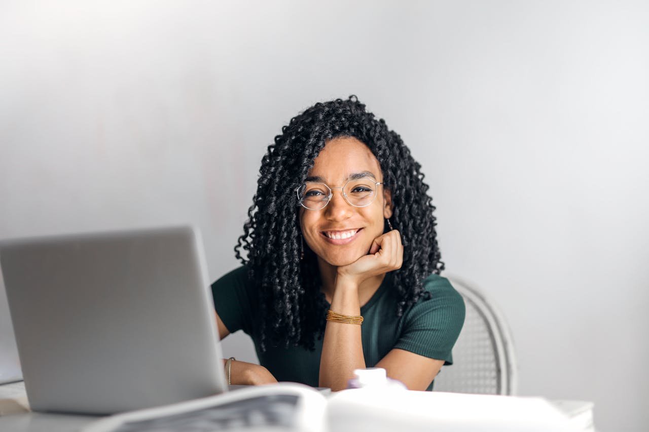 Crafting Captivating Headlines: Your awesome post title goes here Joyful businesswoman with curly hair smiling at camera while using laptop indoors.